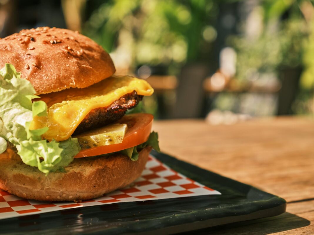 Delicious cheeseburger with lettuce, tomato, and pickles served on a black plate outdoors.