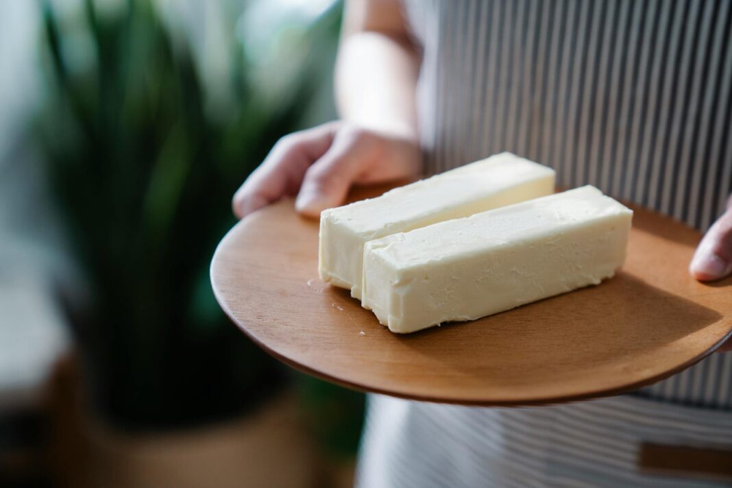 Close-up of hands holding a wooden plate with two sticks of butter.