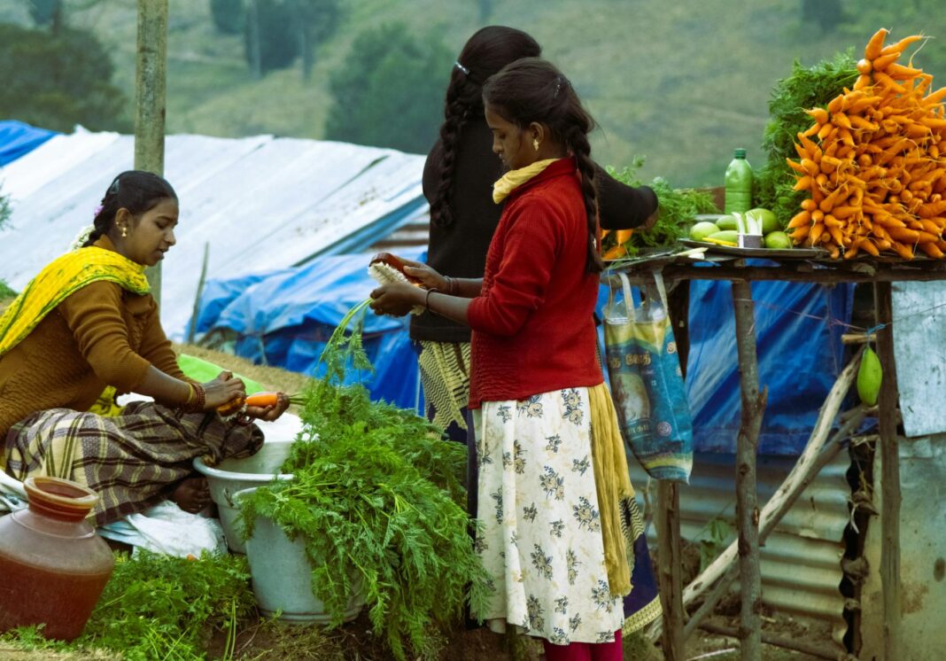 Outdoor market in India with women vendors preparing fresh carrots.